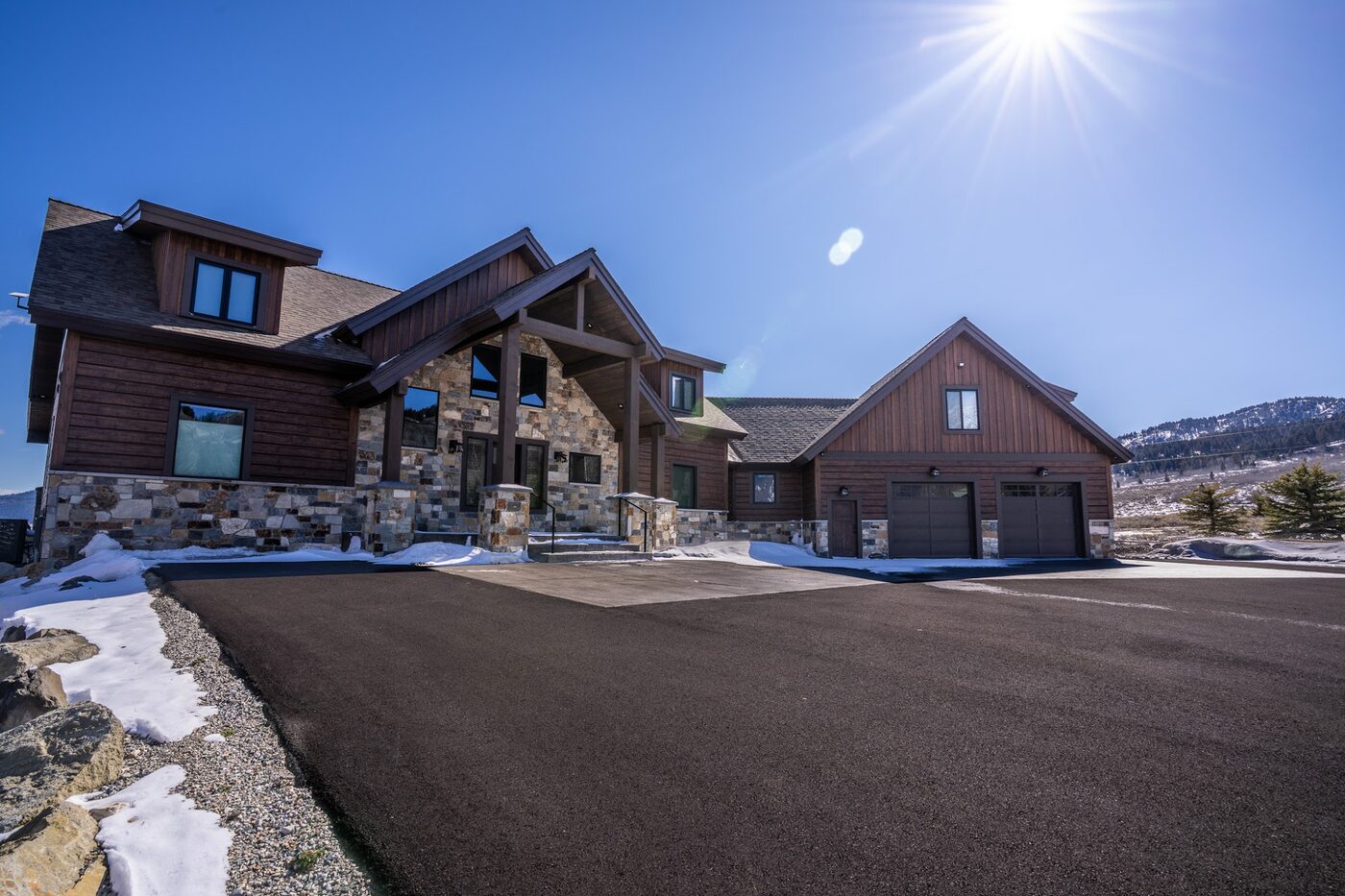 Beautiful Views — front exterior at midday with sun flare and the driveway curving toward the entry