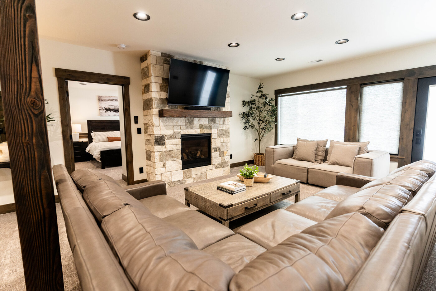 Lodge at Cutthroat Landing — lower-level family room with stone fireplace, sectional, and bedroom beyond