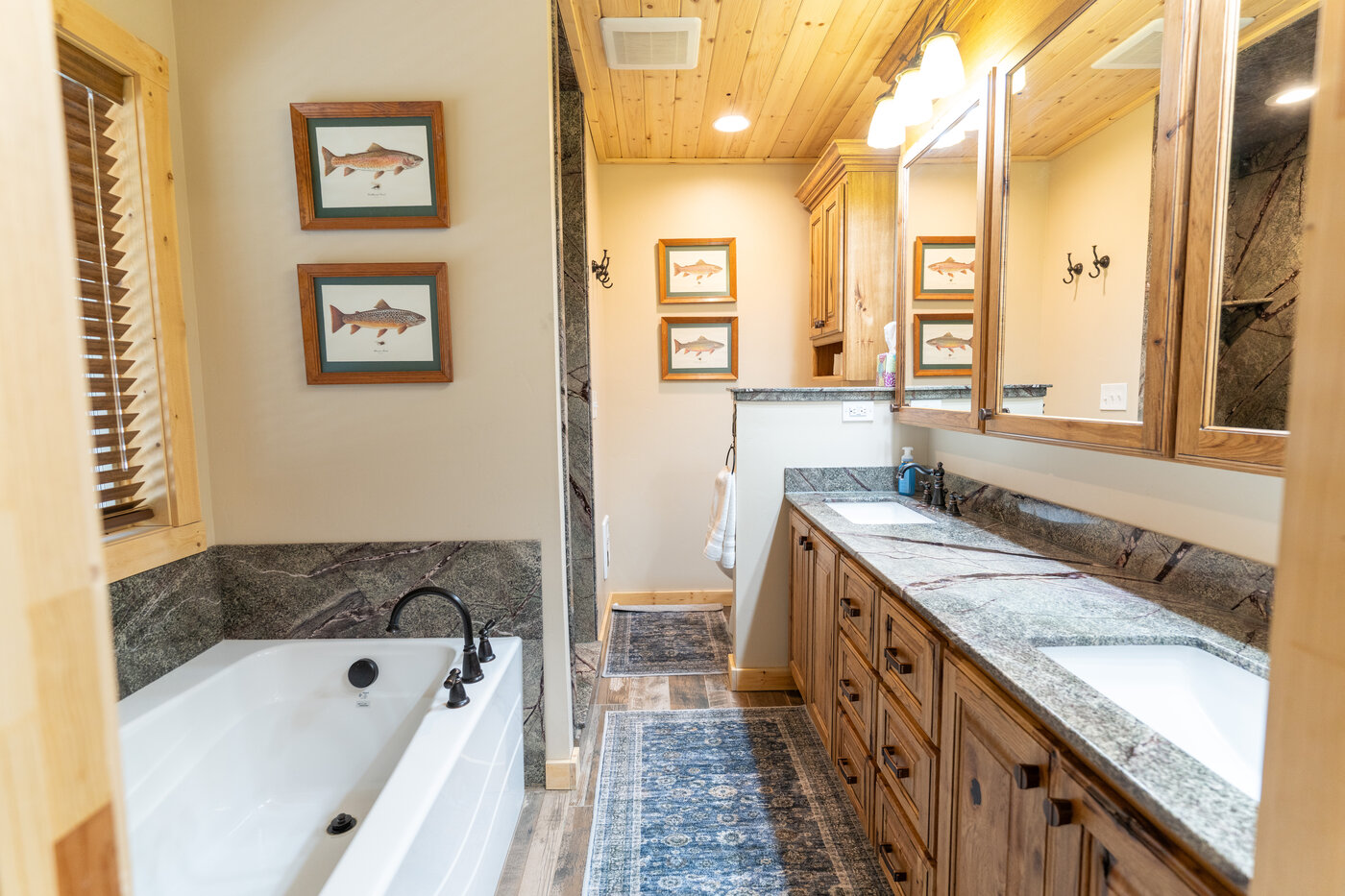 Trails End Lodge — primary bathroom with double-sink granite vanity, soaker tub, and framed fish prints